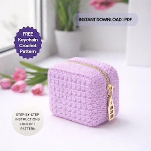 Pode incluir: Uma pequena bolsa de crochê lavanda com um zíper dourado. A bolsa quadrada é feita à mão e apresenta o texto "FREE Keychain Crochet Pattern" e "STEP-BY-STEP INSTRUCTIONS CROCHET PATTERN". A imagem também inclui o texto "INSTANT DOWNLOAD | PDF".