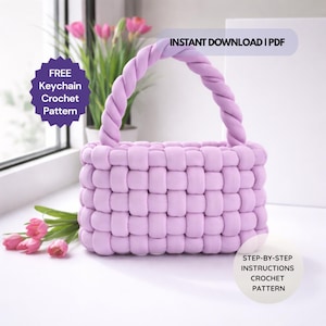 Puede incluir: Un bolso de ganchillo lila tejido con un asa retorcida. El bolso está sobre una superficie blanca, junto a una ventana con tulipanes rosas y una planta. El texto de la imagen dice "FREE Keychain Crochet Pattern" y "INSTANT DOWNLOAD | PDF".