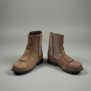 May include: A pair of brown leather ankle boots with side zippers. The boots have a rounded toe and a contrasting light brown panel on the side. The soles are black.