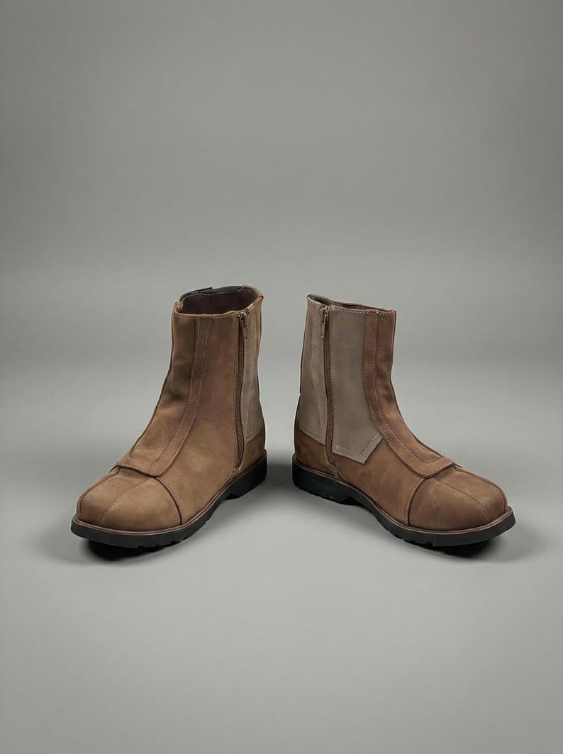 May include: A pair of brown leather ankle boots with side zippers. The boots have a rounded toe and a contrasting light brown panel on the side. The soles are black.