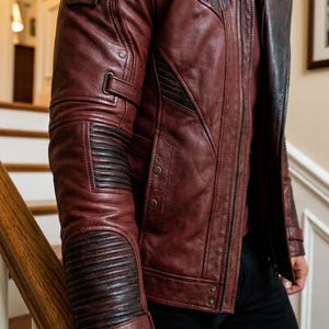 Pu&ograve; includere: Giacca in pelle bordeaux con dettagli neri. La giacca presenta un colletto rialzato, una chiusura con cerniera e pi&ugrave; tasche. Le maniche hanno dettagli a coste sui gomiti e sui polsini. La giacca &egrave; indossata con una camicia rossa e pantaloni neri.