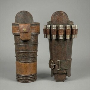 May include: Two brown leather arm bracers. One is a cylindrical shape with a flap and a strap with a button closure. The other is a rectangular shape with a buckle closure and several silver and brown cylinders attached.