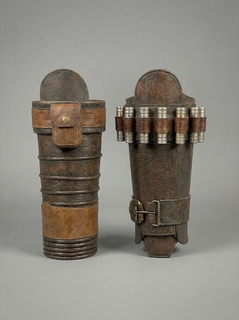 May include: Two brown leather arm bracers. One is a cylindrical shape with a flap and a strap with a button closure. The other is a rectangular shape with a buckle closure and several silver and brown cylinders attached.