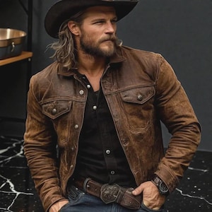 Könnte beinhalten: Braune Lederjacke mit klassischem Design, zwei Brusttaschen und Knopfverschlüssen. Die Jacke wird über einem schwarzen Hemd getragen und mit einem Cowboyhut und Gürtel kombiniert. Der Gesamtstil ist robust und westlich inspiriert.