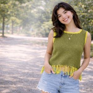 May include: Olive green sleeveless top with yellow trim and fringe. The top is made of a knitted material and is paired with denim shorts. A gold necklace is visible.