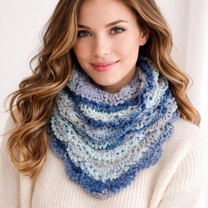 May include: A crocheted cowl in shades of blue, light blue, and grey. The handmade neck warmer has a scalloped edge and is worn around the neck. The cowl is made of soft yarn and is a cosy accessory.