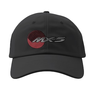 May include: Black baseball cap with a curved brim. The cap features an embroidered design of a red and gray circle with the text "MX-5" in gray. The cap is made of a durable fabric and has a structured fit.