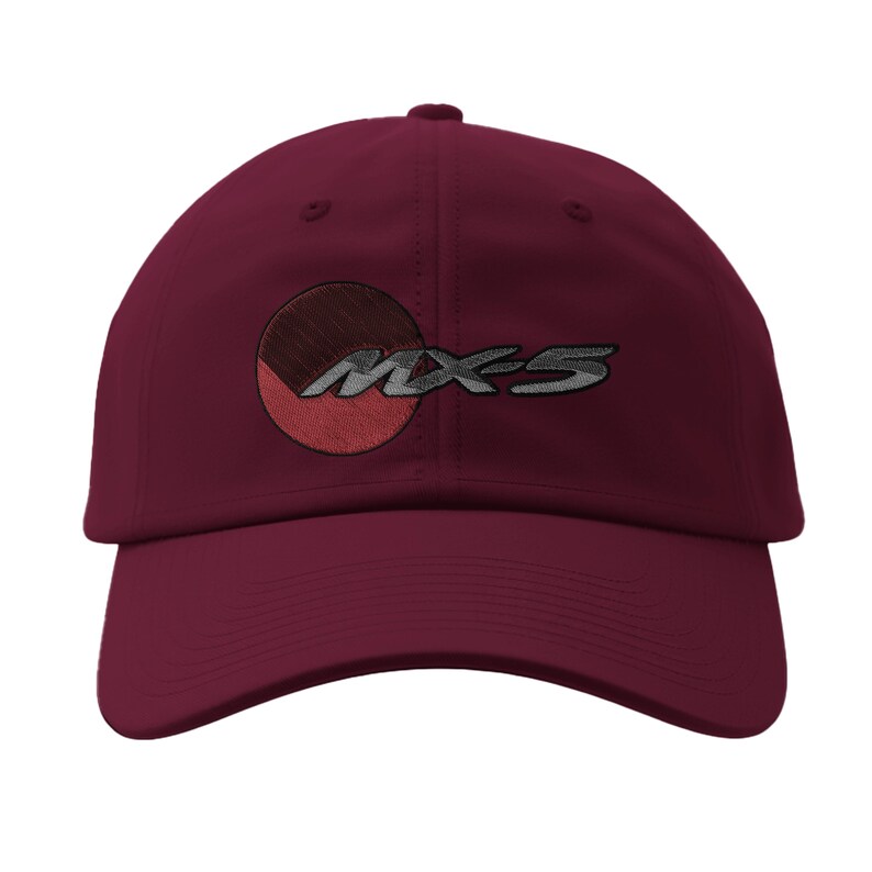 May include: A maroon baseball cap with the embroidered text "MX-5" in silver. The design includes a partial circle with red and brown shading. The cap has a curved brim and a structured crown.