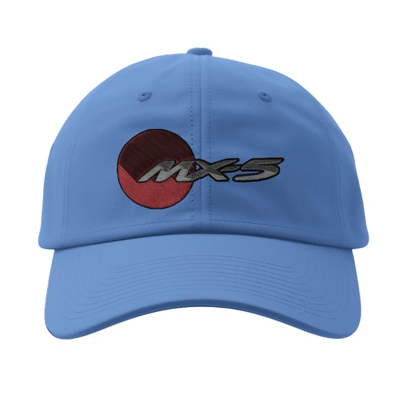 May include: A light blue baseball cap with the embroidered text "MX-5" in silver and a red and brown circle design. The cap has a curved brim and a fabric strap closure.