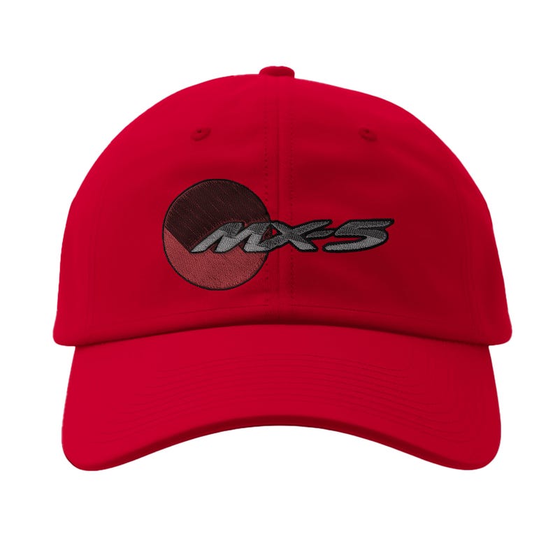 May include: A bright red baseball cap featuring the embroidered text "MX-5" in silver. The design includes a circular emblem with brown and red segments. The cap has a curved brim and a classic six-panel construction.
