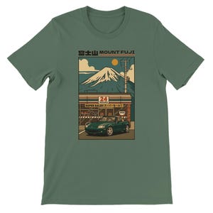 Puede incluir: Camiseta verde con un gráfico del Monte Fuji, un coche verde y una tienda de conveniencia japonesa. El diseño incluye un sol, nubes y una estética retro. El texto "Mount Fuji" está en la parte superior.