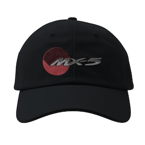 May include: Black baseball cap featuring the embroidered text "MX-5" in silver, with a red and maroon circular design. The cap has a curved brim and a structured crown, suitable for sun protection.