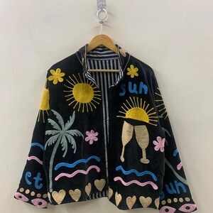 May include: Black jacket with colorful embroidered beach-themed design. Features a yellow sun, palm tree, waves, flowers, champagne glasses, and the word "sun". The jacket has a striped lining.