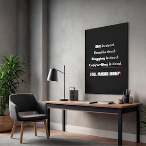 May include: A black framed poster with white text that reads "SEO is dead. Email is dead. Blogging is dead. Copywriting is dead. STILL MAKING MONEY!" is displayed on a gray wall. A black desk lamp, chair, and desk are in front of the poster.