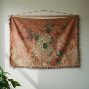 May include: A rectangular tapestry with a floral design in shades of orange, green, and beige hangs from a wooden rod. The tapestry has a fringed edge and is mounted on a white wall. The overall aesthetic is rustic and artistic.