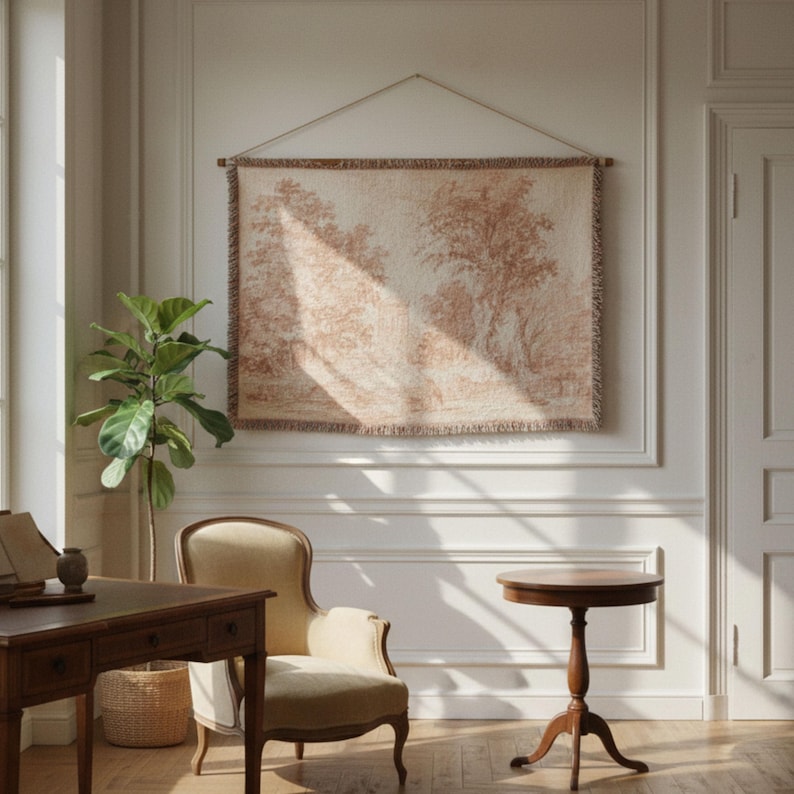 May include: A tapestry depicting a pastoral scene in shades of beige and brown hangs on a white wall. The tapestry is suspended by a wooden rod and a string. The room also features a wooden desk, a chair, and a small round table.