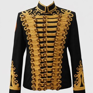 Puede incluir: Chaqueta negra de estilo militar con detalles dorados. Presenta un cuello alto, ribetes de cuerda dorada, botones y bordados dorados en hombros y mangas. El diseño es formal y evoca uniformes militares históricos.