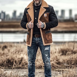 May include: A person wearing a brown and black Carhartt jacket with a tan shearling collar and cuffs, paired with distressed blue jeans and brown boots. The jacket has a small logo patch. The background features a city skyline and dry grass.