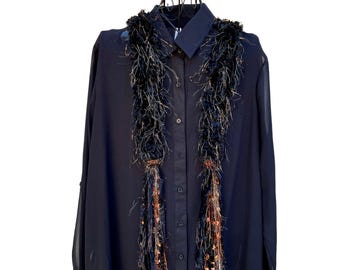 May include: A dark blue button-down shirt with a decorative black and gold scarf. The scarf has a textured, fringed design with copper-coloured accents. The shirt is displayed on a black metal mannequin.