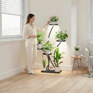 May include: A black metal plant stand with multiple circular shelves, each holding potted plants. The stand has a curved design with built-in lights. The plants include various green foliage and a flowering plant. The stand is indoors near a window.