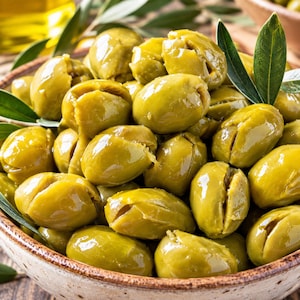 May include: A ceramic bowl filled with numerous pitted green olives, each featuring a distinct vertical slit. The olives have a glossy, smooth texture and a vibrant light green color, accented by several fresh, pointed green olive leaves.