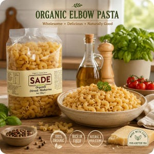 以下が含まれることがあります： Organic Elbow Pasta、Wholesome、Delicious、Naturally Good、Net: 500 g eと書かれたラベル付きのSadeオーガニックエルボーパスタの透明なプラスチック袋。その横には、調理済みのエルボーパスタ、オリーブオイル、チーズが入った陶器のボウルが置かれています。