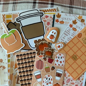 May include: A collection of autumn-themed stickers and activity sheets featuring illustrations of pumpkins, caramel apples, ghosts, coffee cups, and acorns. The items include a bingo card labeled Autumn Adventures, a grid of acorns, and various die-cut stickers.