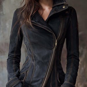 Puede incluir: Chaqueta vaquera negra con cremallera diagonal y cuello con solapas. La chaqueta presenta costuras color canela visibles y una silueta entallada. Las mangas tienen puños abotonados, estilo motero clásico.