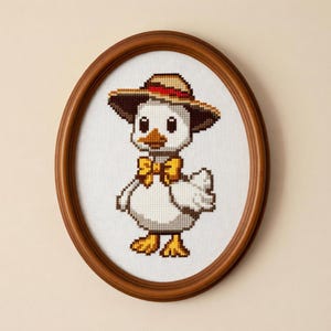 May include: Cross-stitch artwork of a duck wearing a brown hat with a red band and a yellow bow tie. The duck is framed in an oval, wooden frame. The duck has white feathers, a yellow beak, and yellow feet.