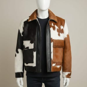Könnte beinhalten: Zweifarbige Kuhfelljacke. Die linke Seite zeigt ein schwarz-weißes Muster, während die rechte Seite ein braun-weißes Muster aufweist. Sie hat einen Kragen, zwei Vordertaschen und eine schwarze Lederverkleidung.