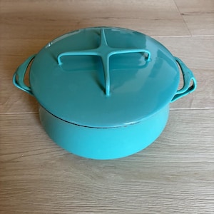 以下が含まれることがあります： ターコイズ色のダッチオーブンと、お揃いの蓋。 蓋には十字型のハンドルと、持ち運びやすいように両側にハンドルが付いています。 丸い形で、鋳鉄製のように見えます。