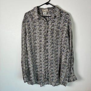 May include: A long-sleeve button-down shirt featuring a repeating geometric pattern in shades of tan, brown, and dark blue. The shirt has a standard collar, a front button placket, and a label at the neckline that reads MONTAGE.