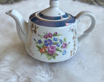 Tetera de porcelana japonesa vintage de alta calidad con acabado floral brillante y detalles dorados azules.