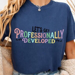 Pode incluir: Uma t-shirt azul-marinho de manga curta com o texto "LET'S GET PROFESSIONALLY DEVELOPED" impresso numa fonte multicolorida e divertida. A t-shirt tem um decote redondo e é combinada com calções de ganga azul-claros para um visual casual.