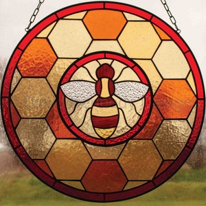 Pode incluir: Dois painéis de vitral com um design de abelha estilizado. O painel superior mostra uma abelha com as asas abertas sobre um fundo de favo de mel vermelho e amarelo. O painel inferior mostra uma abelha em um círculo rodeado por um design de favo de mel maior.