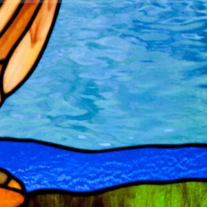 Pu&ograve; includere: Una finestra in vetro colorato con un paesaggio blu e verde. La parte superiore della finestra presenta un design astratto in tonalit&agrave; di marrone, arancio e giallo.