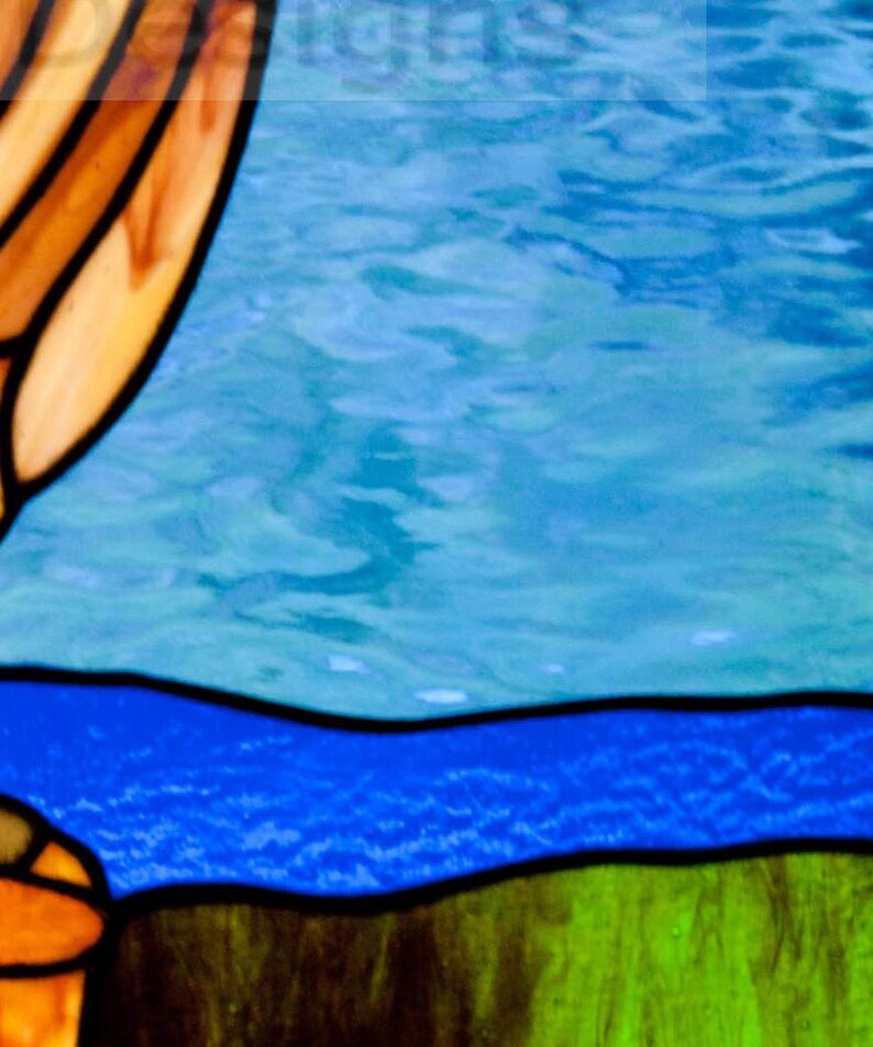 Pu&ograve; includere: Una finestra in vetro colorato con un paesaggio blu e verde. La parte superiore della finestra presenta un design astratto in tonalit&agrave; di marrone, arancio e giallo.