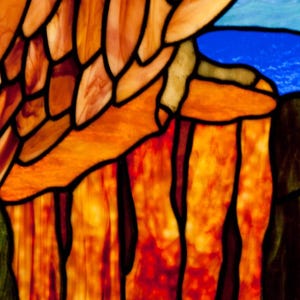 Pu&ograve; includere: Primo piano di una finestra in vetro colorato con pezzi di vetro arancio, giallo e rosso. Il vetro &egrave; disposto in un motivo di linee verticali e file orizzontali. Il vetro &egrave; illuminato da dietro, creando un bagliore caldo.