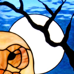 Pu&ograve; includere: Un'opera d'arte in vetro colorato che raffigura un gufo con una grande luna bianca sullo sfondo. L'occhio del gufo &egrave; visibile e la luna &egrave; circondata da un ramo d'albero nero.