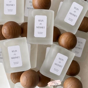 May include: A collection of rectangular frosted glass bottles with rounded wooden spherical caps. Each bottle features a white rectangular label printed with the text SELIN & MEHMET and the date 02.05.2026. A small pink tag reads GIFTS FOR EVERYONE.