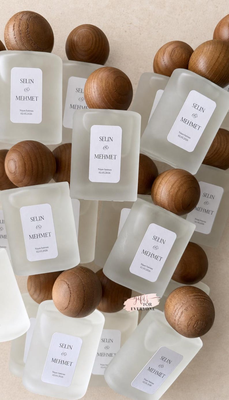 May include: A collection of rectangular frosted glass bottles with rounded wooden spherical caps. Each bottle features a white rectangular label printed with the text SELIN & MEHMET and the date 02.05.2026. A small pink tag reads GIFTS FOR EVERYONE.