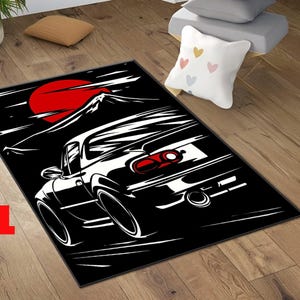 May include: Black rectangular rug with a white car graphic, a red sun, and a mountain silhouette. The rug has the text "C-1" in red in the lower left corner. The car is depicted from the rear, with its taillights visible.