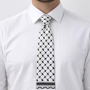 May include: A white tie with a black geometric pattern, worn with a white dress shirt. The tie features a repeating grid of black dots and lines, with a decorative border at the bottom.