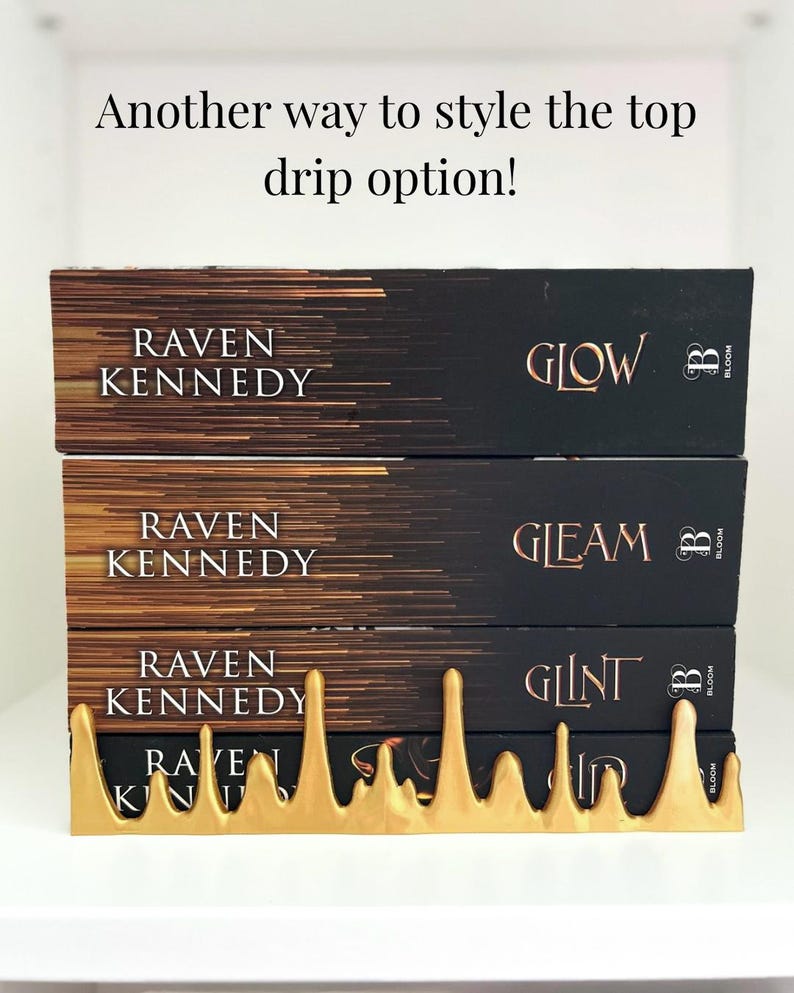 May include: A stack of three books with black covers and gold lettering, titled "Glow", "Gleam", and "Glint" by Raven Kennedy. A gold-colored, stylized drip design holds the books in place. The text "Another way to style the top drip option!" is at the top.