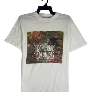 May include: White t-shirt with a jungle scene graphic featuring a bear and a black panther. The text "Microsoft Dangerous Creatures" is printed on the front. The shirt is hanging on a black hanger.
