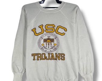 May include: Off-white USC Trojans sweatshirt with the university's logo in gold and brown. The logo includes the letters "USC", the words "University of Southern California", and the word "Trojans". The sweatshirt has long sleeves and a crew neck.