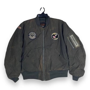 May include: A dark olive green bomber jacket with a zip-up front, ribbed cuffs, and a ribbed hem. The jacket features patches on the chest and sleeve, including a U.S. Air Force patch and a patch with the text "University of Toledo".