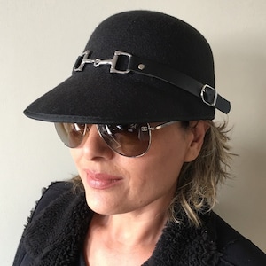 May include: A black felt hat with a wide brim and a silver horse bit buckle on the front. The hat has a black leather strap with a silver buckle on the side.