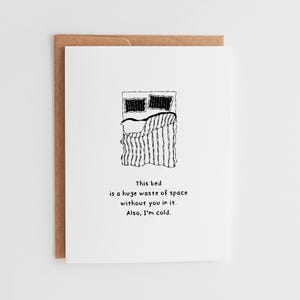 May include: A white greeting card with a brown envelope. The card features a black and white illustration of a bed with pillows and a striped blanket. Text on the card reads: "This bed is a huge waste of space without you in it. Also, I'm cold."