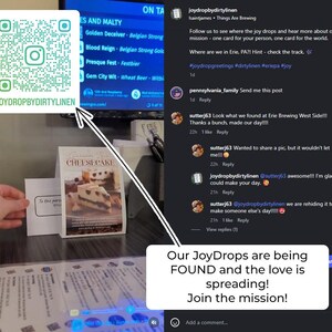 May include: A white square card featuring a teal Instagram QR code and the text JOYDROPBYDIRTYLINEN, positioned next to a small table tent sign displaying a cheesecake image and the text CHEESECAKE, alongside a social media interface overlay.